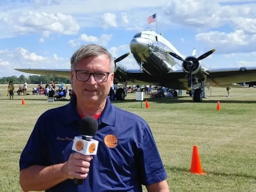 A man holding a microphone in front of an airplane.