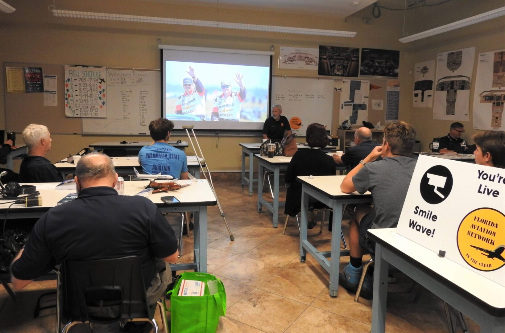 A group of people sitting at tables in front of a projector screen.