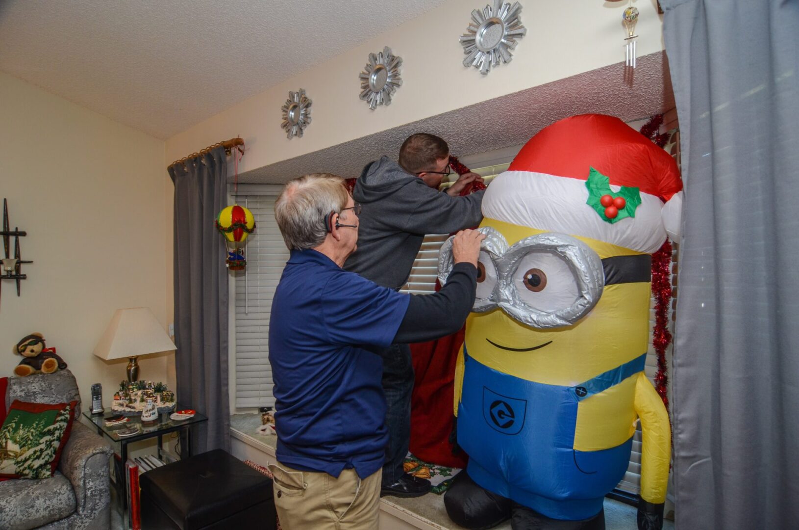 A man and two boys putting up a minion christmas decoration.