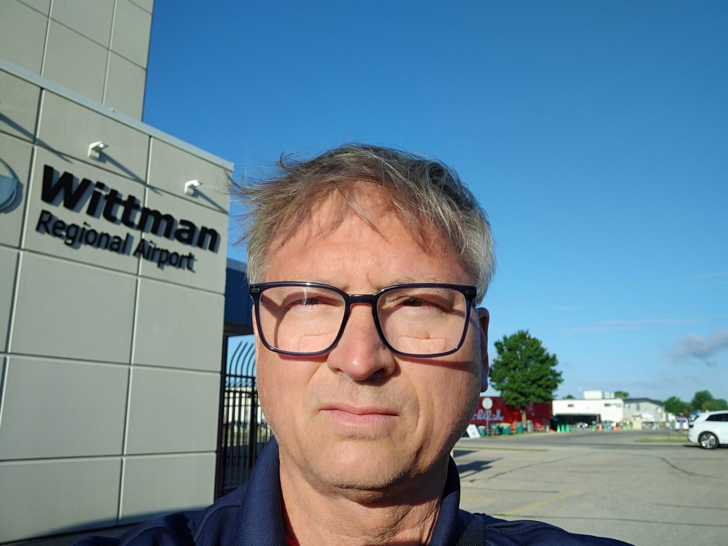 A man with glasses standing in front of an airport.