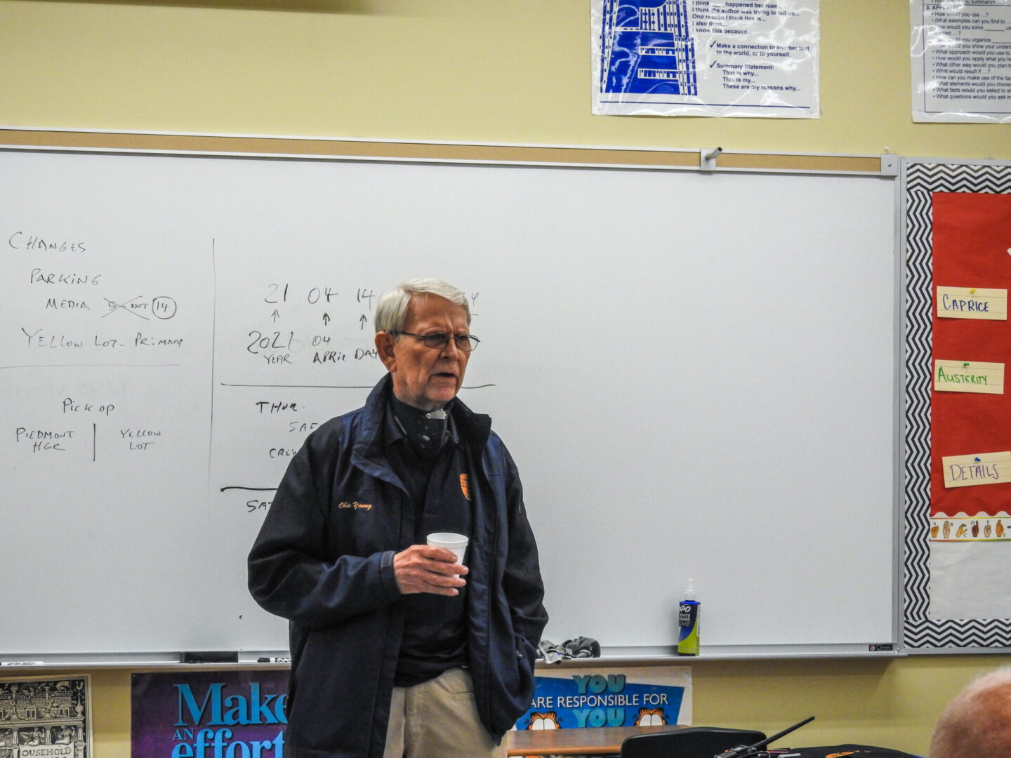 A man standing in front of a whiteboard holding a cup.