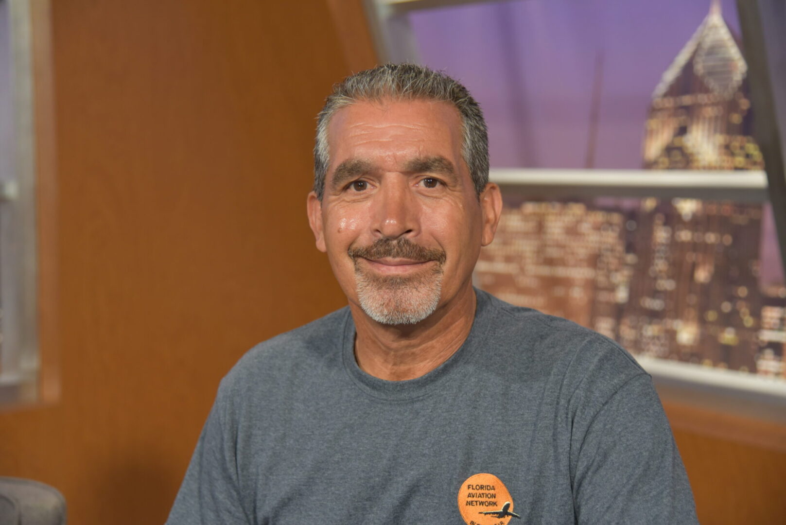 A man with grey hair and mustache wearing a blue shirt.