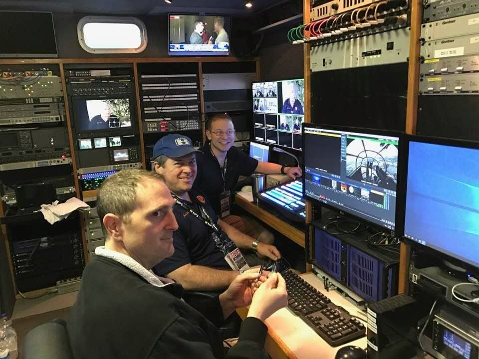 Three men are sitting in front of a computer.