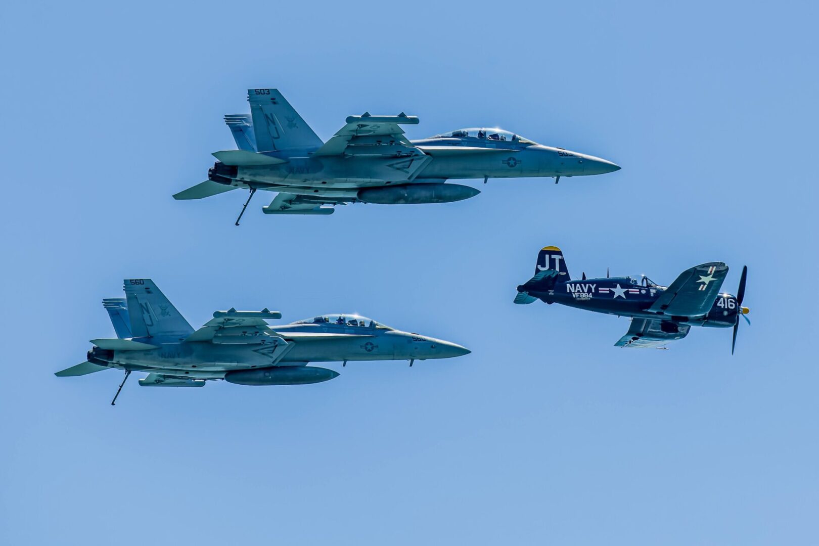 Two jets flying in formation with a fighter jet behind them.