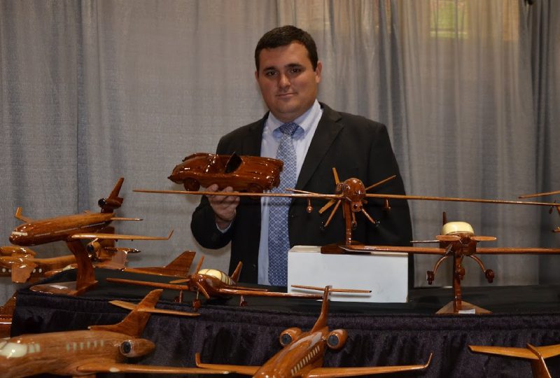 A man standing in front of wooden planes and cars