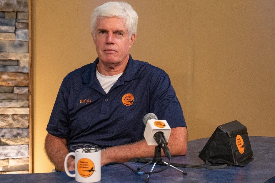 Man sitting at table with microphone, mug.