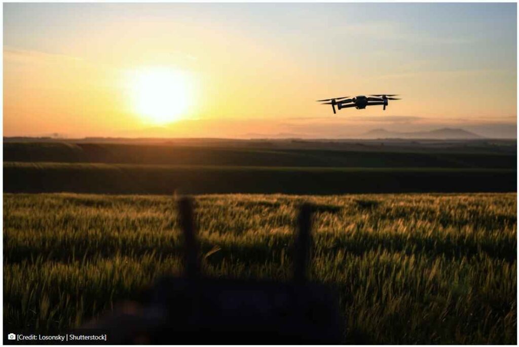 Drone flying over field at sunset.